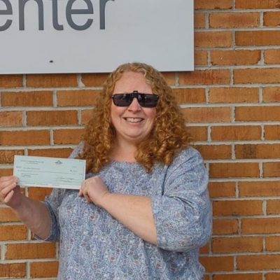 smiling woman in dark sunglasses stands in front of brick wall with check